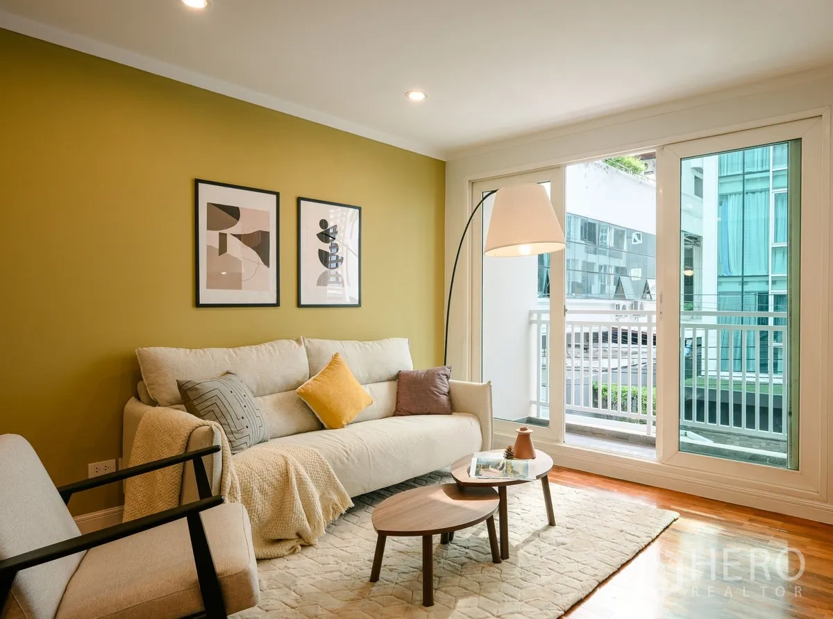 公寓 for sale in Watthana, Bangkok - 沙发布置在落地玻璃旁，通往小阳台，可见外部建筑景观。