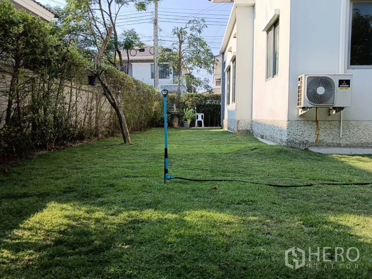 独立式住宅 出售在Lat Krabang, Bangkok - 侧院草坪配绿篱，外机与浇灌水管可见。