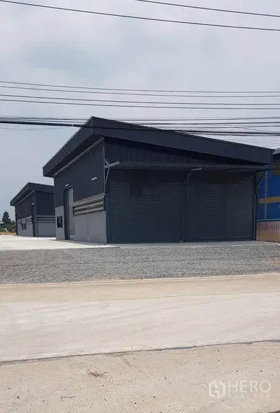 货栈 出租在Lat Lum Kaeo, Pathum Thani - 成排深色新仓库临街而立，前方有电力线。