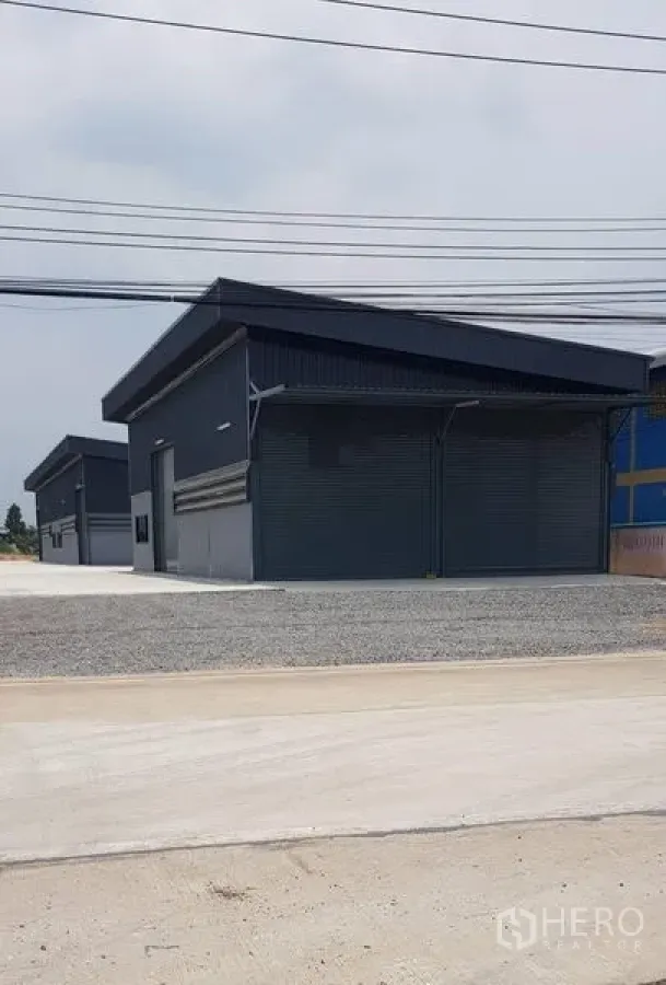 货栈 出租在Lat Lum Kaeo, Pathum Thani - 成排深色新仓库临街而立，前方有电力线。