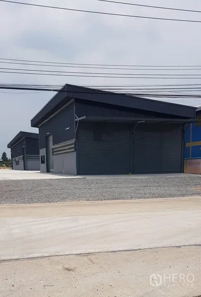 货栈 出租在Lat Lum Kaeo, Pathum Thani - 成排深色新仓库临街而立，前方有电力线。