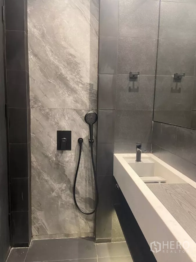 Townhouse for rent in Huai Khwang, Bangkok - Modern bathroom with gray tiles, handheld shower and a long white trough sink.