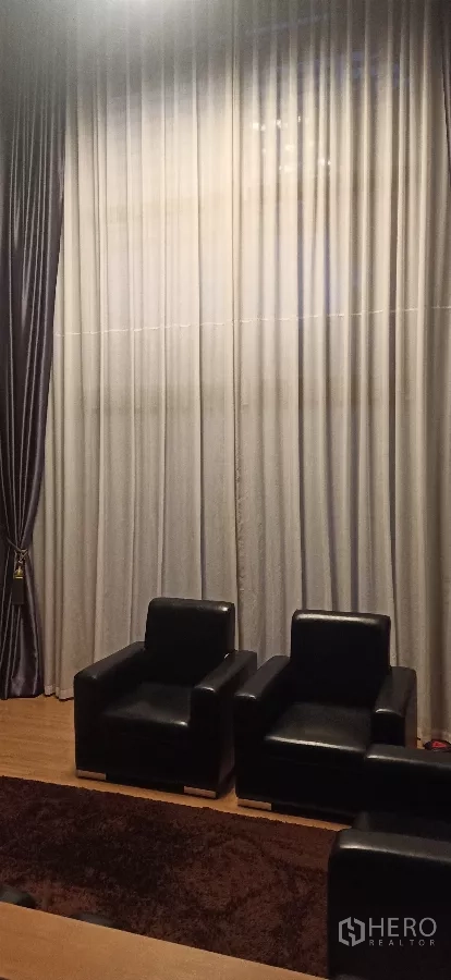Detached House for rent or sale in Khan Na Yao, Bangkok - Double-height sitting area with sheer curtains and two black lounge chairs.