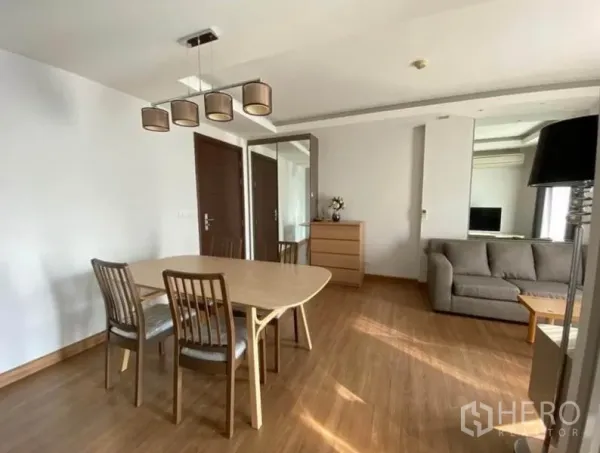 Condominium for rent in Huai Khwang, Bangkok - Dining table and chairs beside a sofa in a bright condo living room with wood flooring.