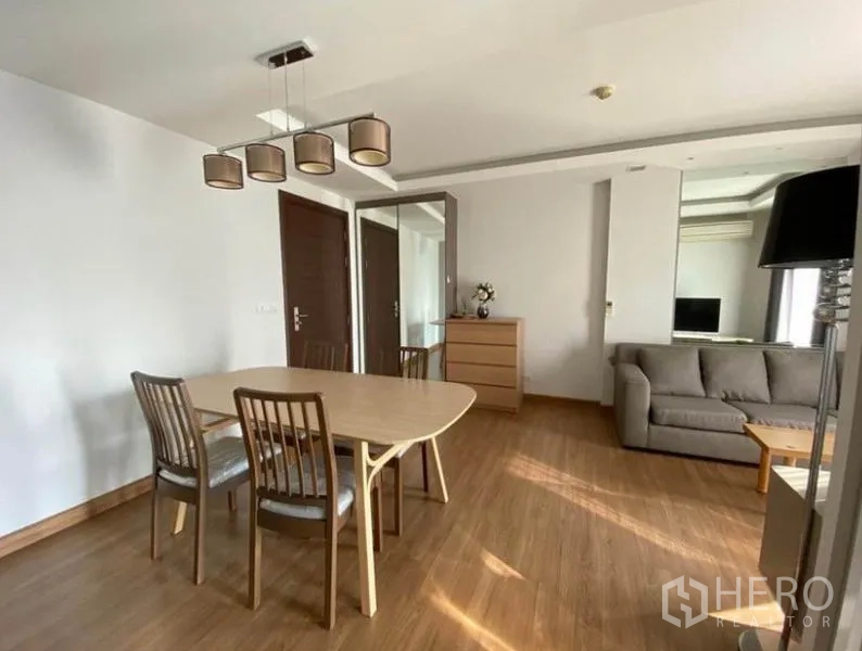 Condominium for rent in Huai Khwang, Bangkok - Dining table and chairs beside a sofa in a bright condo living room with wood flooring.