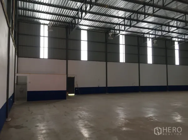 Warehouse for rent in Pathum Thani - Interior corner with tall vertical windows and a small office/restroom section inside the warehouse.