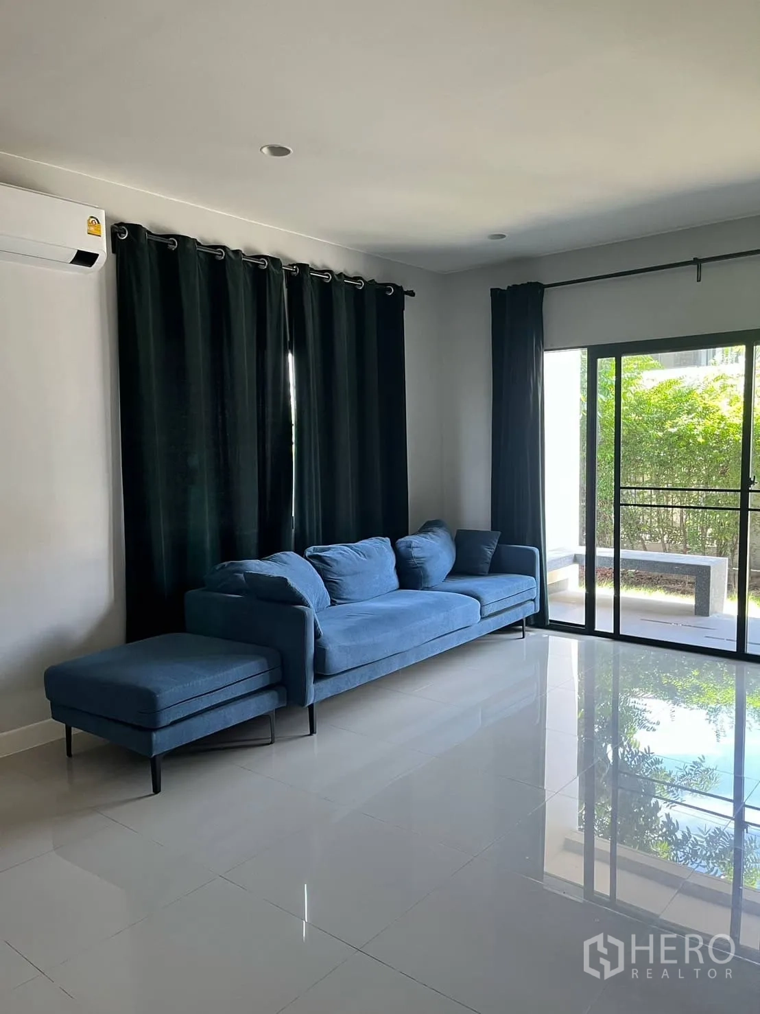 Detached House for rent or sale in Lam Luk Ka, Pathum Thani - Bright living room with blue sectional sofa, glossy tiles and sliding glass door to patio.