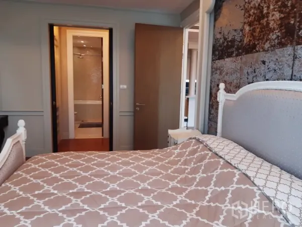 Condominium for rent in Khlong Toei, Bangkok - Bedroom view toward the ensuite bathroom with textured accent wall and wooden door.