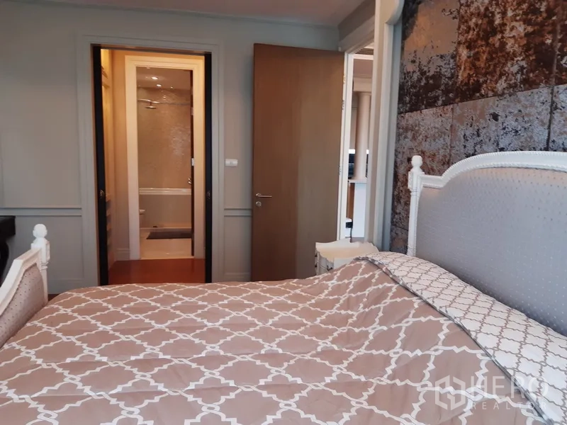 Condominium for rent in Khlong Toei, Bangkok - Bedroom view toward the ensuite bathroom with textured accent wall and wooden door.
