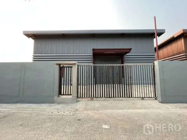 Warehouse for rent in Khlong Sam Wa, Bangkok - Front view of grey steel-clad warehouse with sliding gate and paved driveway offering truck access.