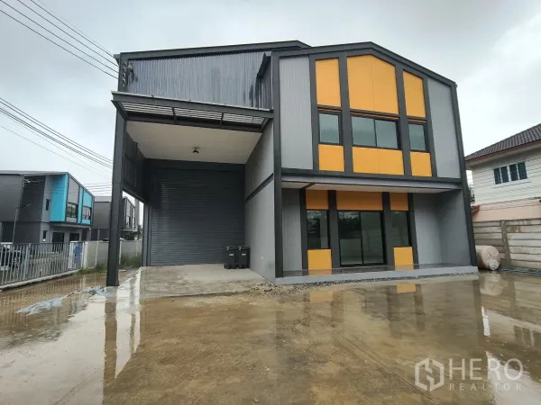 Warehouse for rent or sale in Bang Yai, Nonthaburi - Modern warehouse exterior in grey and orange with two‑storey office, covered loading bay, large roller shutter and concrete yard.