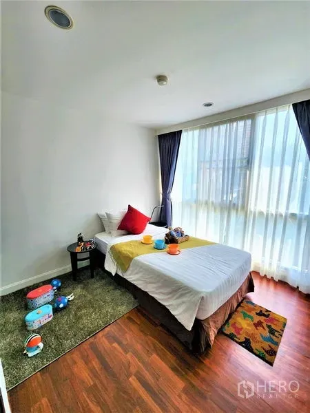 Condominium for rent in Bang Rak, Bangkok - Sunlit single bedroom with floor-to-ceiling curtains and warm wood flooring.