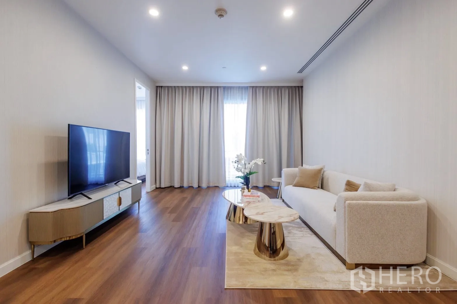 คอนโด for rent or sale in Pathum Wan, Bangkok - ห้องนั่งเล่นพร้อมโซฟา ชั้นวางทีวี และผ้าม่านสูงจรดเพดาน