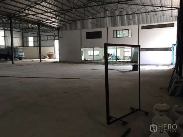Warehouse for rent in Saphan Sung, Bangkok - Spacious warehouse interior with high steel trusses, concrete floor, and a built-in office block with glass windows.