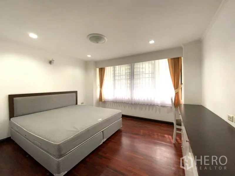 公寓 出租在Watthana, Bangkok - 宽敞卧室，铺木地板，配大床、大窗及长条内置书桌。