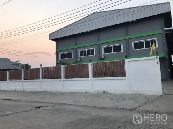 Factory for sale in Pak Kret, Nonthaburi - Side view of the gray factory with metal roof, windows, and perimeter wall.