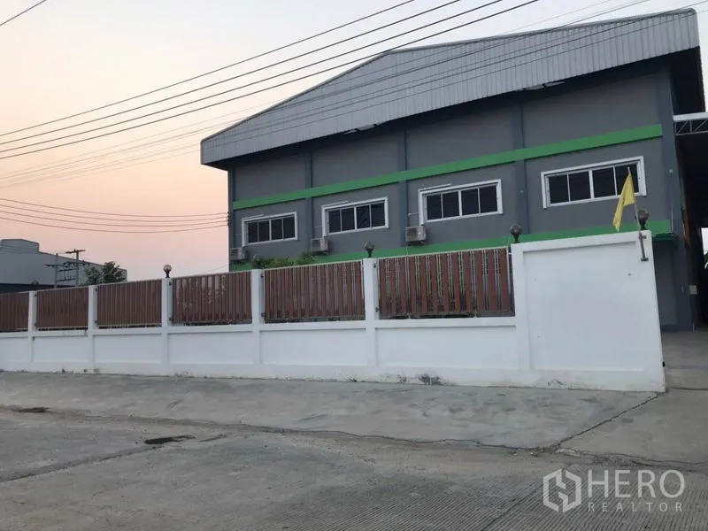 Factory for sale in Pak Kret, Nonthaburi - Side view of the gray factory with metal roof, windows, and perimeter wall.
