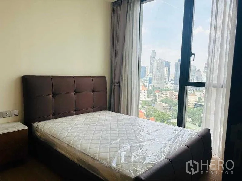 Condominium for rent in Khlong Toei, Bangkok - Bedroom with upholstered headboard, mattress, and floor-to-ceiling corner windows.