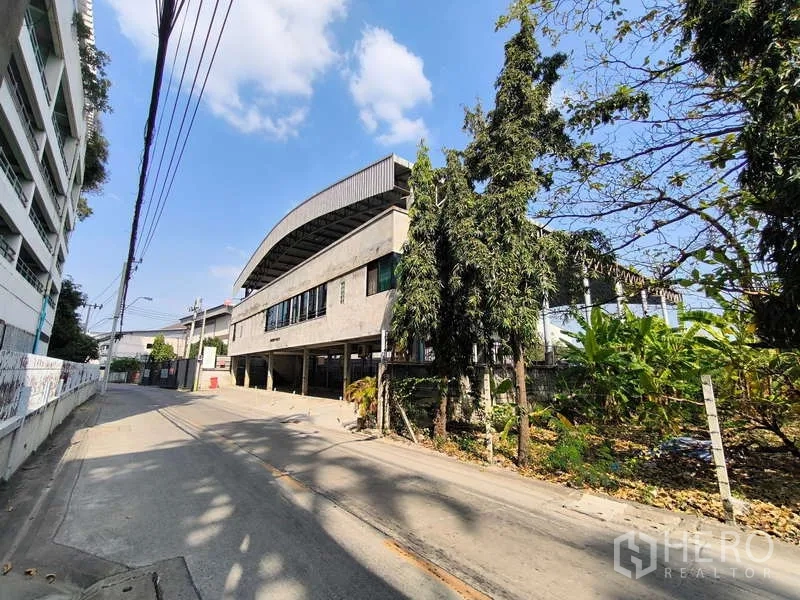 货栈 出租在Huai Khwang, Bangkok - 绿化环绕的仓库式建筑外立面与安静小路。