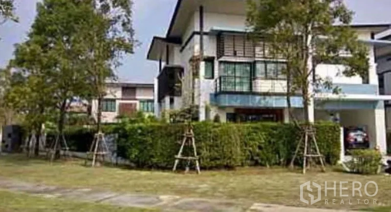 Detached House for sale in Saphan Sung, Bangkok - Modern two-storey house exterior with lawn, tall trees and a hedged corner plot.