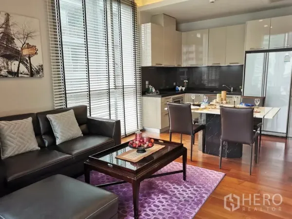 Condominium for rent in Watthana, Bangkok - Bright open‑plan living room with leather sofa, purple rug, sleek kitchen and dining island beside floor‑to‑ceiling windows.