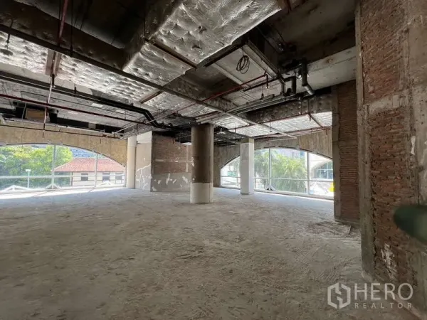 Retail Space for rent - Spacious unfinished shop space with high ceilings, visible MEP lines and street-facing arched windows overlooking greenery.