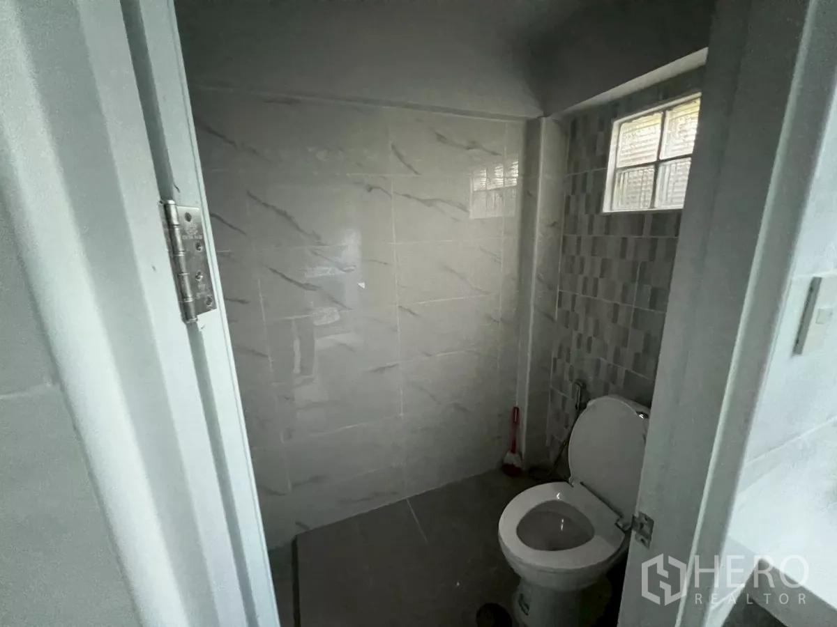 Shophouse for rent in Khlong Toei, Bangkok - Compact bathroom with tiled walls, toilet and glass-block window for ventilation.