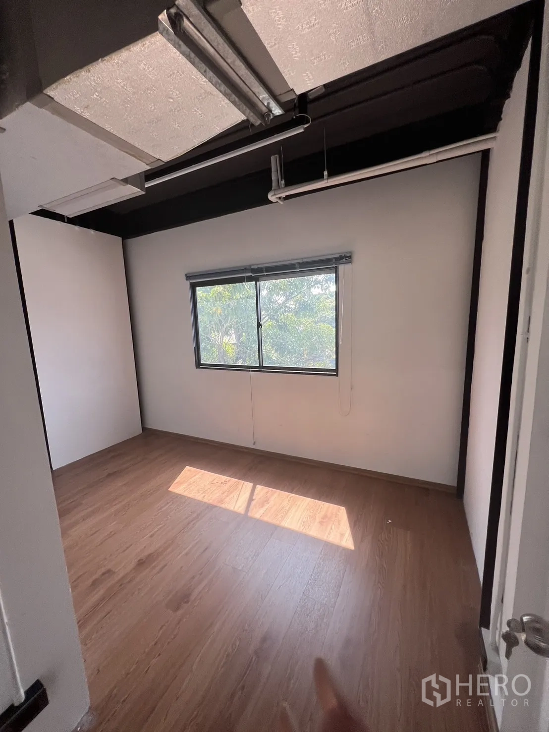 Office Space for rent in Khlong Toei, Bangkok - Compact office with window overlooking greenery, dark ceiling accents and wood floors.