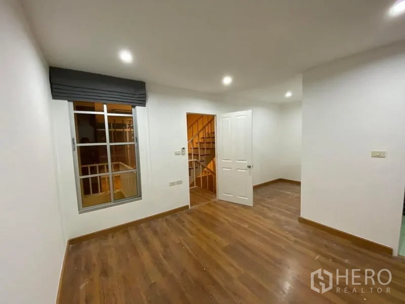 Townhouse for rent in Lat Phrao, Bangkok - Bright bedroom with wood floors, window and doorway opening to the stair landing.