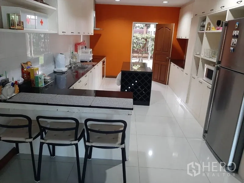 带办公室的家 出售在Phra Khanong, Bangkok - 宽敞现代厨房，白色橱柜、吧台座椅与橙色特色墙。