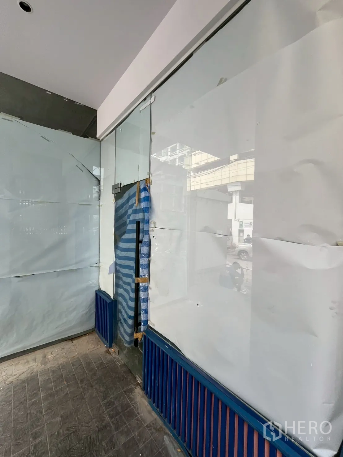 พื้นที่ขายของ for rent in Watthana, Bangkok - ระยะใกล้ประตูกระจกทางเข้าพื้นที่ค้าปลีก ปิดกระดาษชั่วคราว ฐานตกแต่งน้ำเงินส้ม พื้นกระเบื้องมีเงาสะท้อนถนน