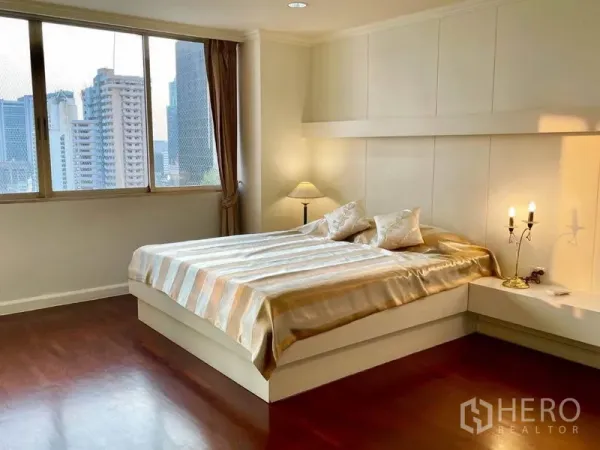 公寓 出租或出售在Watthana, Bangkok - 主卧配大床与墙面装饰，床头灯，眺望城市天际线。