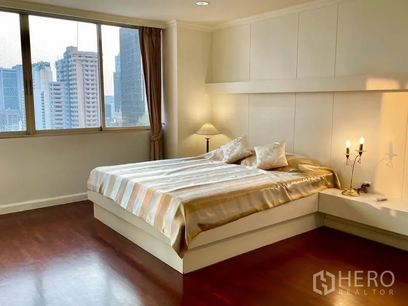 公寓 出租或出售在Watthana, Bangkok - 主卧配大床与墙面装饰，床头灯，眺望城市天际线。