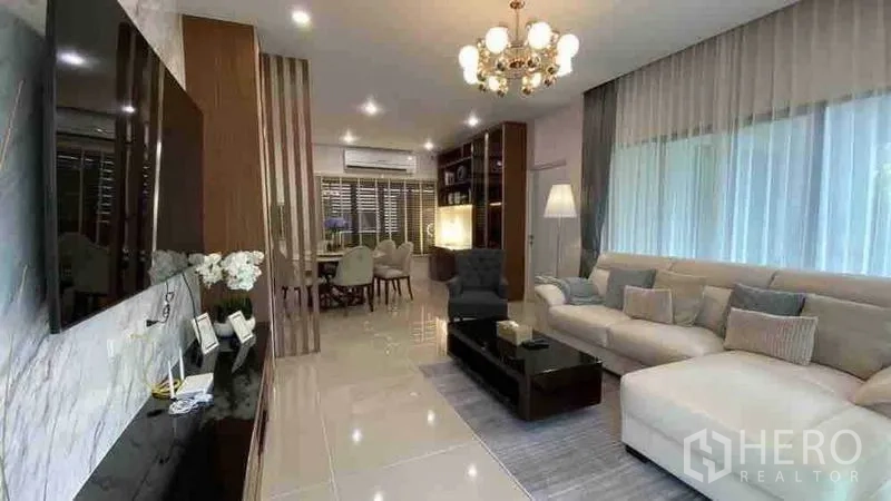 Detached House for rent or sale in Prawet, Bangkok - Spacious living and dining area with L-shaped sofa and sheer curtains.