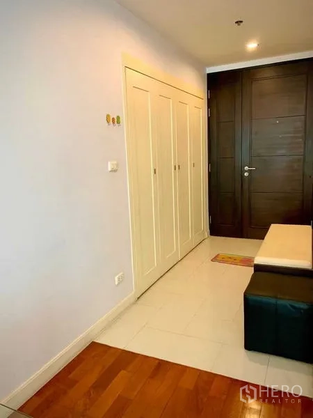 Condominium for rent in Khlong Toei, Bangkok - Entry hallway with built-in white closets, bench and dark wooden front door.