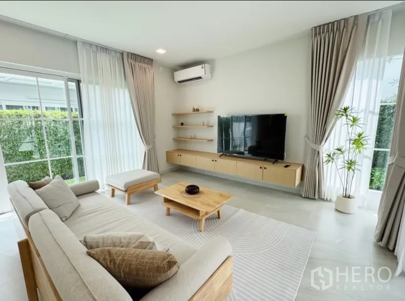 บ้าน ให้เช่าในBang Phli, Samut Prakan - ห้องนั่งเล่นสว่างด้วยโซฟารูปตัวแอล ชุดทีวี และหน้าต่างสูงจรดเพดาน