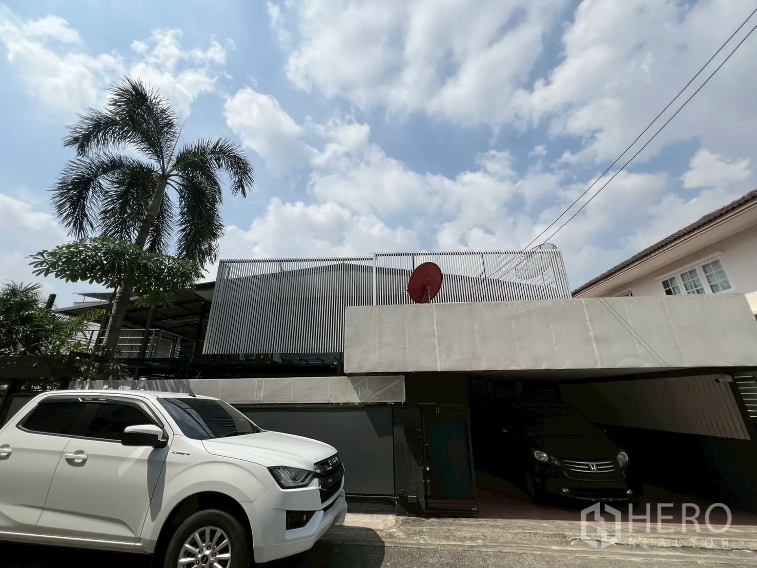Detached House for rent or sale in Wang Thonglang, Bangkok - Street view showing the house’s high fence, covered carport and a palm tree.