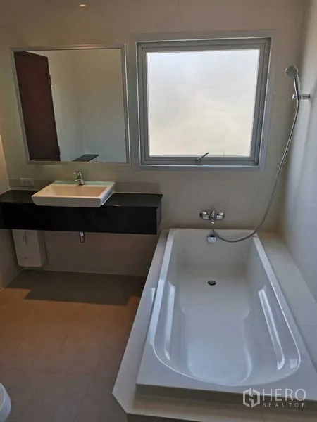Condominium for rent in Khlong Toei, Bangkok - Modern bathroom with soaking bathtub, vanity sink and window bringing natural light.