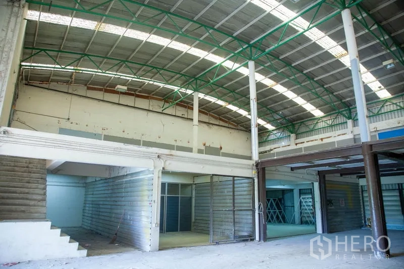 Warehouse for rent in Prawet, Bangkok - Spacious warehouse hall with high arched roof, green steel trusses and mezzanine storage areas.