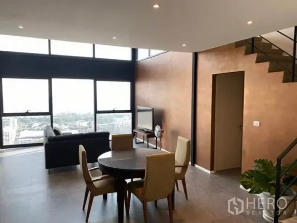Condominium for rent in Bang Rak, Bangkok - Loft-style living and dining area with double-height windows, staircase, and Bangkok city views.
