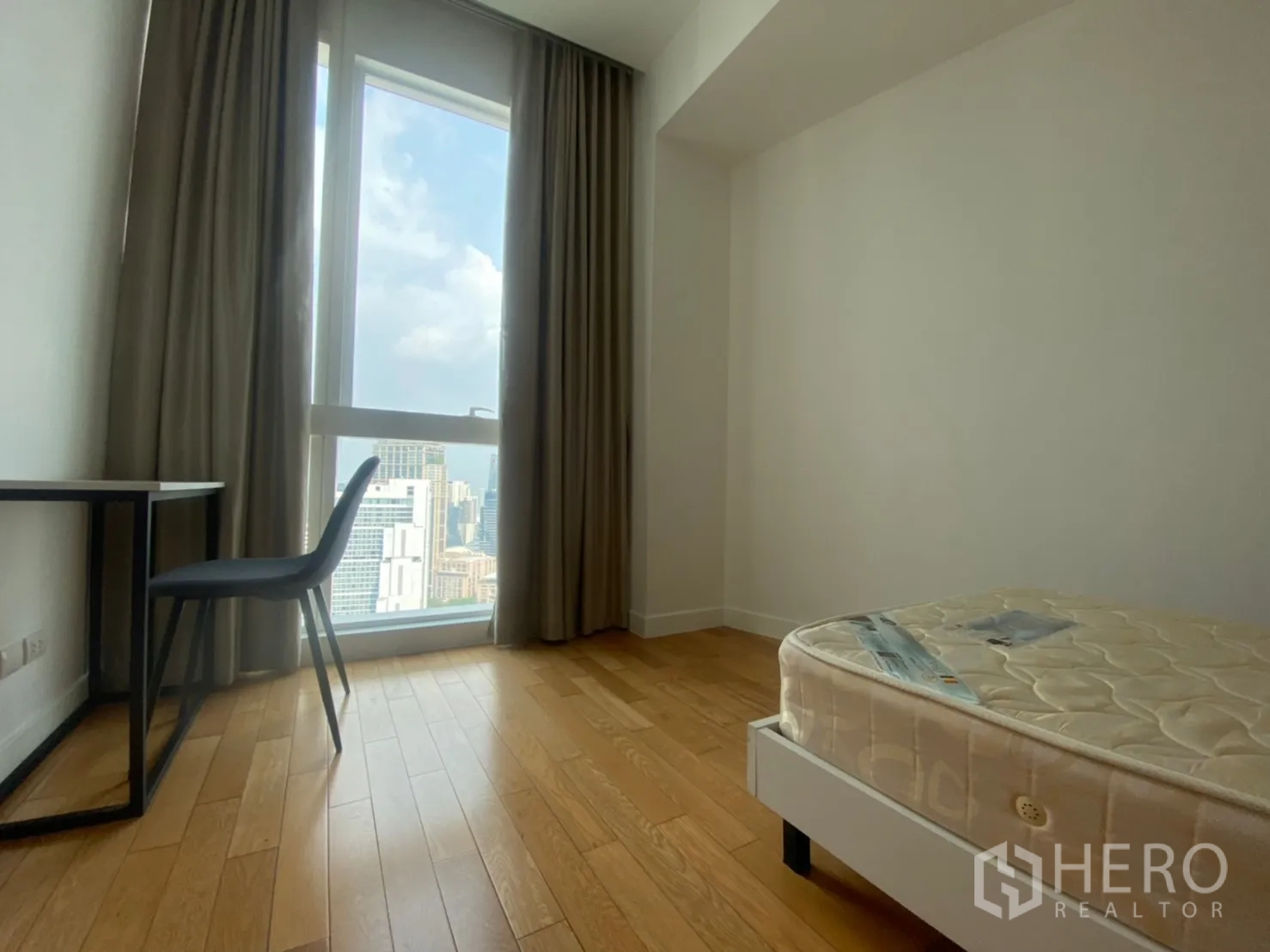 Condominium for rent or sale in Khlong Toei, Bangkok - Second bedroom corner with study desk by a tall window and curtains overlooking the skyline.