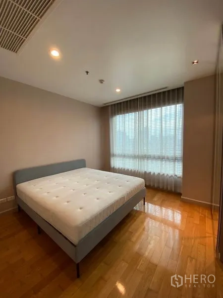 Condominium for rent or sale in Yan Nawa, Bangkok - Corner bedroom with queen bed, sheer curtains and warm wood flooring.