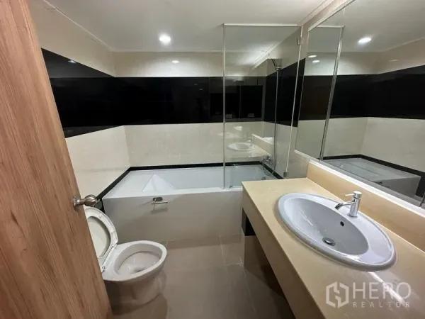 คอนโด ให้เช่าในWatthana, Bangkok - ห้องน้ำที่สองพร้อมอ่างอาบน้ำ ฉากกั้นกระจก กระเบื้องโทนอบอุ่น และอ่างล้างหน้าเคาน์เตอร์กว้าง