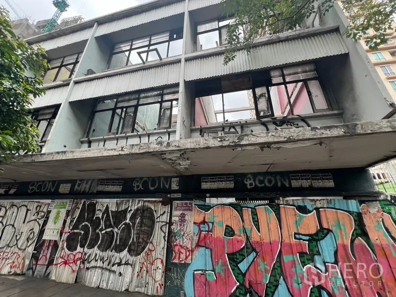 Land for rent in Watthana, Bangkok - Abandoned three-storey building with broken windows and graffiti along the sidewalk.