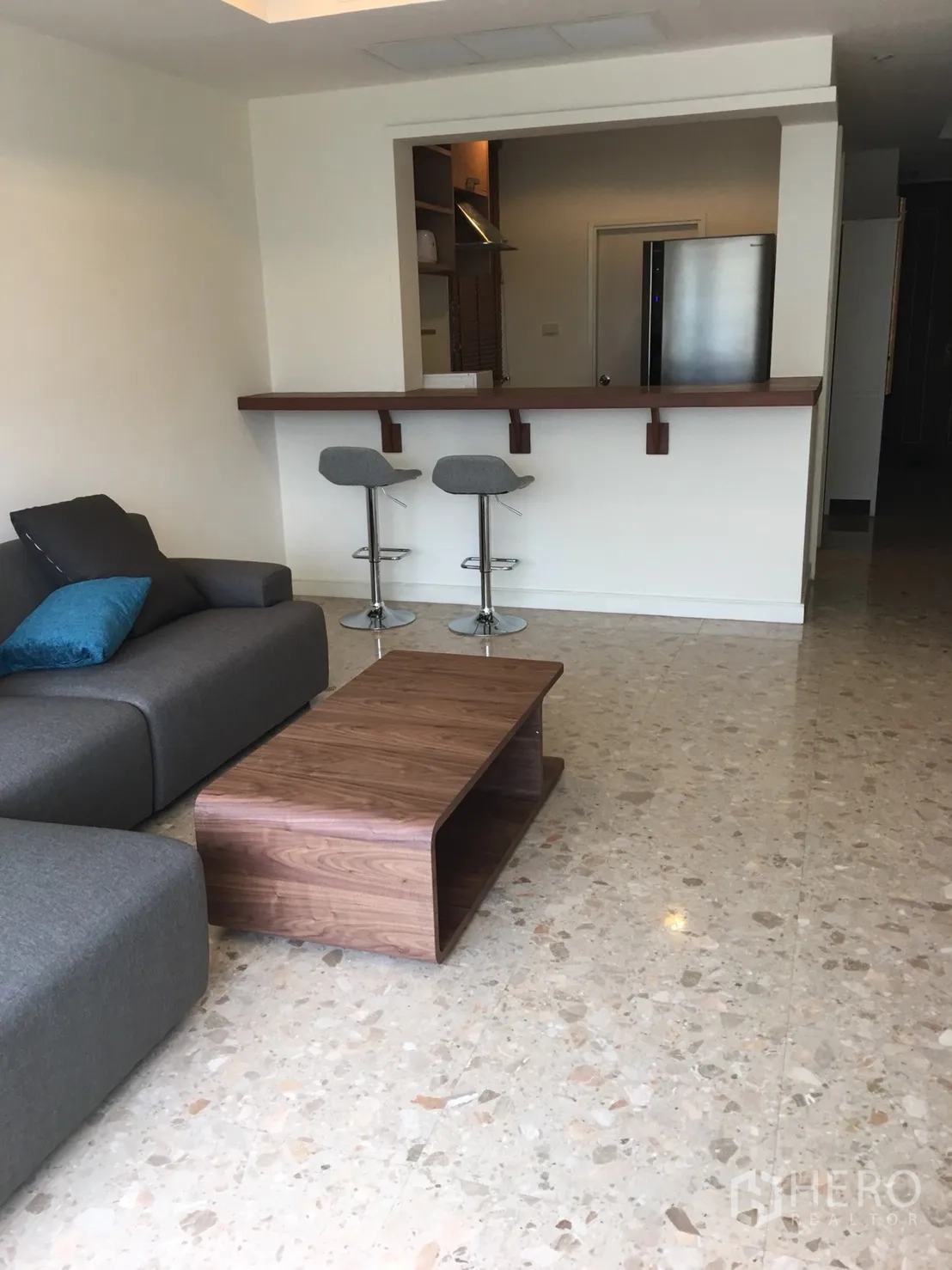 Condominium for rent in Watthana, Bangkok - Living area with gray sofa, wooden coffee table and breakfast bar with stools.