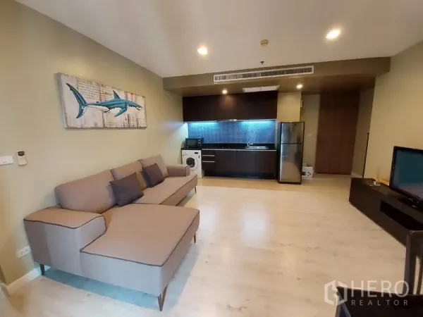 Condominium for rent in Phaya Thai, Bangkok - Open-plan living room with L-shaped sofa, sleek dark kitchenette, washer and stainless fridge.
