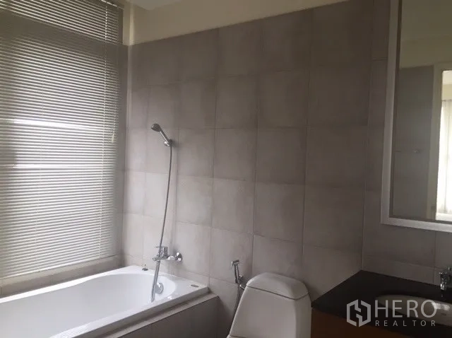 Condominium for rent in Watthana, Bangkok - Bathroom with gray tiles, bathtub and handheld shower beside a window.