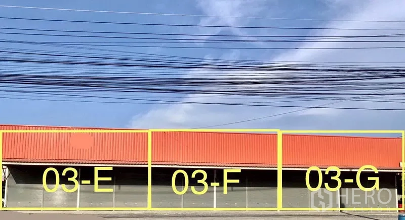 Warehouse for rent in Pathum Thani - Row of warehouse units with an orange roof and multiple roller‑shutter bays marked 03‑E, 03‑F, and 03‑G along a wide frontage.