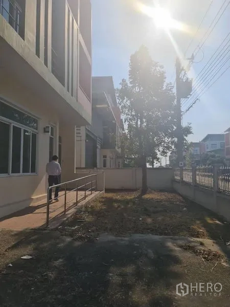 工厂 出租或出售在Lam Luk Ka, Pathum Thani - 前庭与步道、树木及围墙，在下午阳光下。