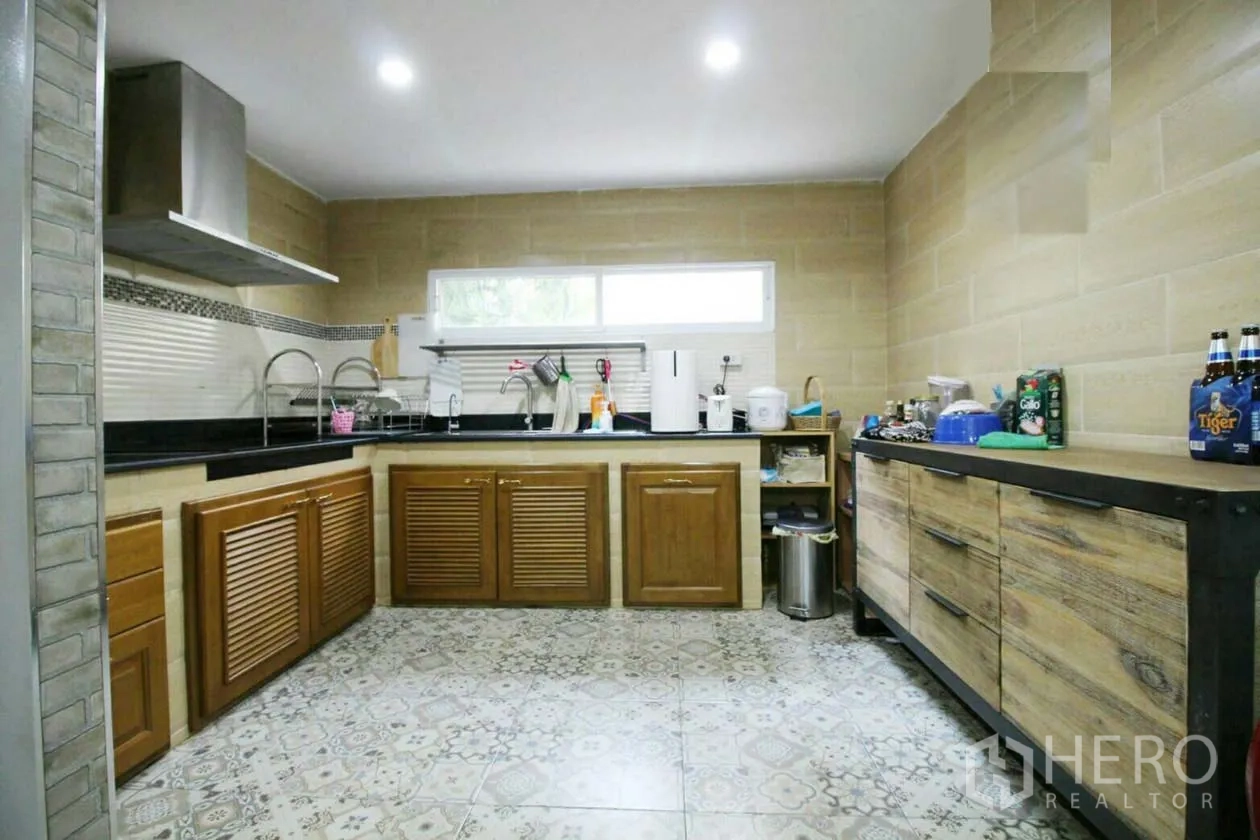Detached House for rent or sale in Lat Krabang, Bangkok - L-shaped kitchen with wood cabinets, patterned floor tiles, window and stainless range hood.